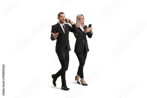 Full length shot of a young businessman and businesswoman walking and using smartphones photo