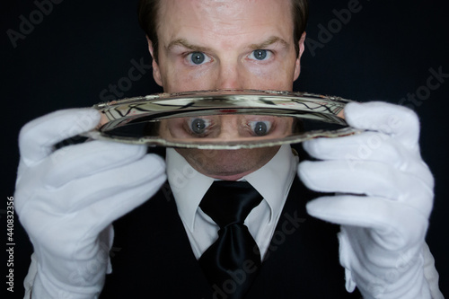 Obraz na plátně Portrait of Butler or Waiter in White Gloves Holding Silver Serving Tray Next to His Face
