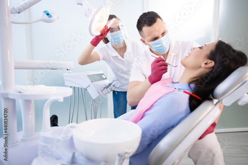 Two dentists treat the teeth of a young patient. Woman sitting in a dental chair. Healthcare  medicine