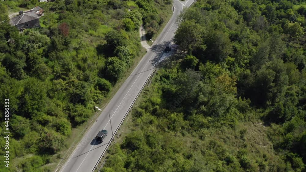 Automobile drives along grey asphalt road among green forestry mountainous landscape to sea under bright sunlight summer aerial top view Automobile drives along grey asphalt road among green forestry mountainous landscape to sea under bright sunlight summer aerial top view