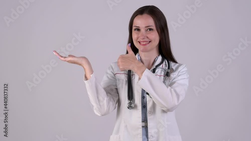 Young Female Doctor in medical Uniform pointing index finger aside on empty palm showing thumb up like. Medical workers showing advertising area for commercial text, copy space on hand.