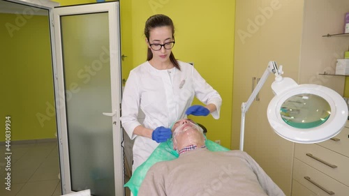 Cosmetologist working with mature patient during biorevitalization treatment. Doctor showing aged client ampoule of hyaluronic acid and explaining anti aging procedure process photo