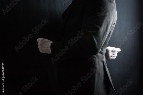 Portrait of Butler or Servant in Dark Suit and White Gloves Standing at Exquisite Attention on Black Background. Service Industry and Professional Hospitality. © jeremyimagery.com