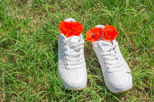 White sneakers on green grass in summer, red poppies inside. The concept of neutralizing sweat odors in shoes after wearing
