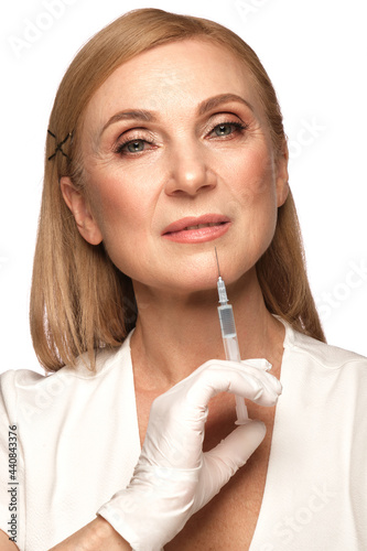 Portrait of a beautiful elderly woman in a white shirt with classic makeup and blond hair with syringe in hands photo