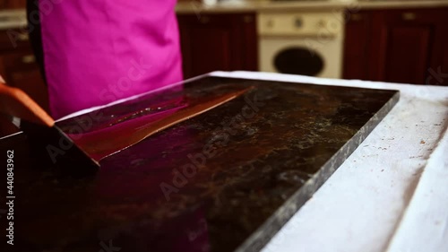 Top view video shows a chocolatier woman stirring tempered liquid dark chocolate on a marble table using a cake scraper to cool it and prepare delicious chocolates. photo