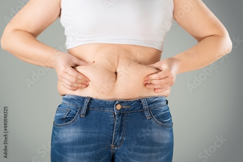Woman in jeans and shirt squeezing her belly fat. Dieting and fat loss concept.
