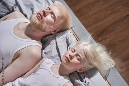 Tableau sur toile Girl laying at the bed with closed eyes near her bearded albino father and relax