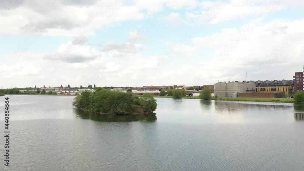rising above lake and revealing buildings. Green trees on islet in middle of water surface. Cloudy sky rising above lake and revealing buildings. Green trees on islet in middle of water surface. Cloudy sky