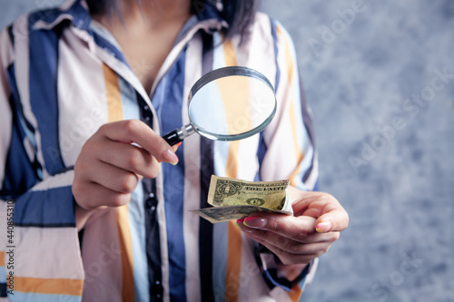 young woman looking at money with a magnifying glass