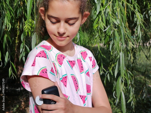 Girl with diabetes checks glucose level in blood with device for continuous glucose monitoring – CGM. She is reading glucose level from the white sensor on right arm. Insulin depend. Diabetes type 1. photo