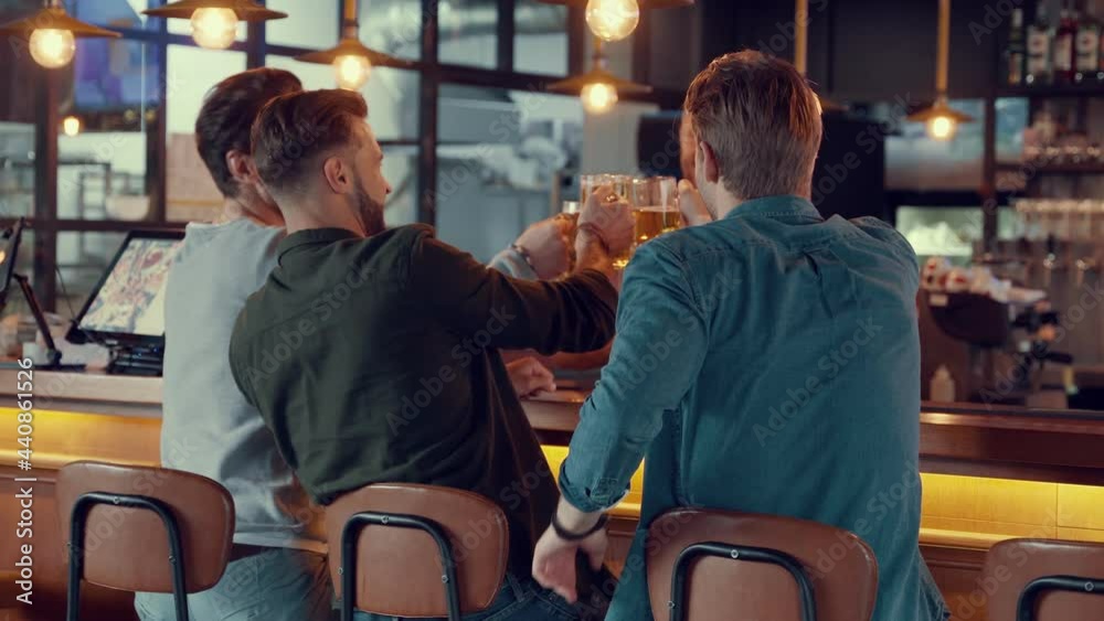 Rear view of happy young men toasting each other with beer in the pub Rear view of happy young men toasting each other with beer in the pub