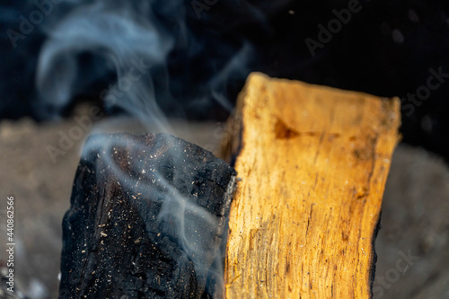 Photo of a mesquite dried-wood log emitting smoke and of a newly added kiln dried cooking wood in a fire pit on a sunny day of June 20, 2021. photo