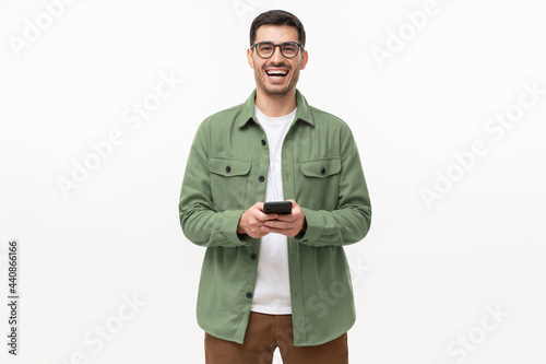 Young happy man laughing as he is looking at camera, holding his phone, isolated on gray background