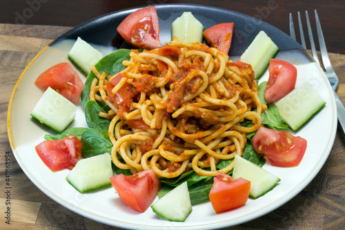 spaghetti and tomato sauce over spinach greens with sliced tomato and cucumber 