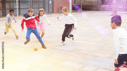 Cheerful tween schoolchildren gaily spending time together on warm spring day, playing with ball near school building. © JackF