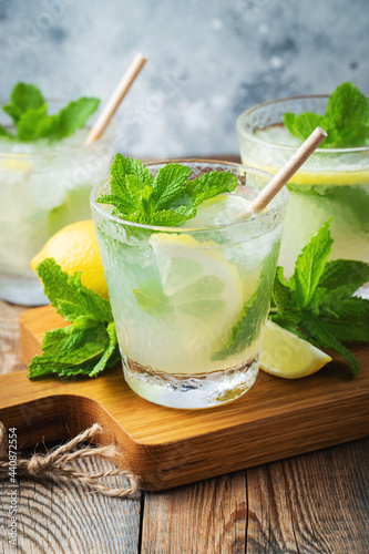 Two glass with lemonade or mojito cocktail with lemon and mint, cold refreshing drink or beverage with ice on rustic blue background