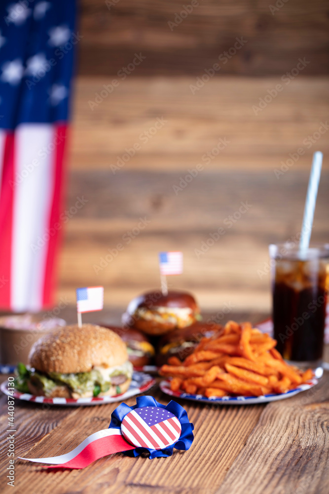 Fourth of July celebration. American flag and decorations. Burgers on rustic wooden table.
Fourth of July celebration. American flag and decorations. Burgers on rustic wooden table.