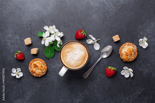 Cup of coffee with cakes and spring flowers on dark stone background. Top view