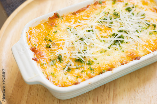 Close up and selective focus baked cheesy italian classic homemade food,lasagna with topping of vegetable and parmesan cheese served in wooden plate looks delicious menu for dinner or lunch.