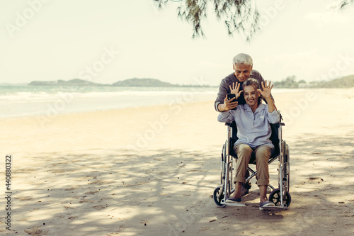 retired couple Husband pushes a wheelchair to his wife The couple was happy at the sandy beach. Retirement couple concept and health care.