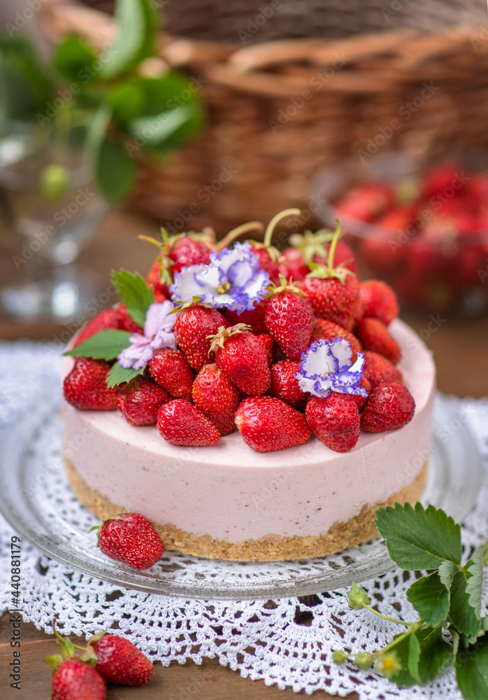 Strawberry cheesecake with a decor of a large number of strawberries and violet flowers lying on a lace napkin on a wooden background Strawberry cheesecake with a decor of a large number of strawberries and violet flowers lying on a lace napkin on a wooden background