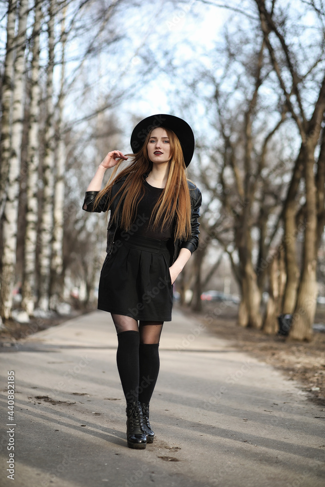 Young beautiful girl in a hat and with a dark make-up outside. Girl in the Gothic style on the street. A girl walks down the city street in a leather waistcoat with a phone. Young beautiful girl in a hat and with a dark make-up outside. Girl in the Gothic style on the street. A girl walks down the city street in a leather waistcoat with a phone.