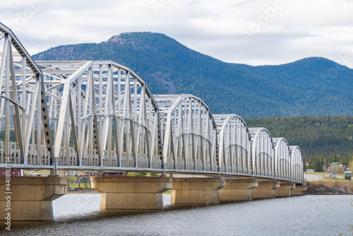 Large man made structure steel bridge spanning across Nisutlin Bay in township of Teslin flowing to the Yukon River in northern Canada during spring summer time with cloudy mountains background. photo