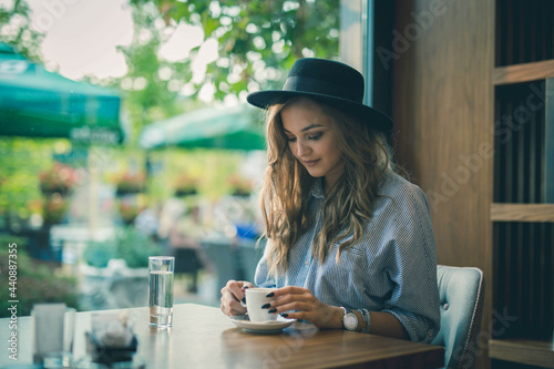 Cheerful beautiful Bosnian Caucasian woman in a hat holding a cup of coffee in a cafe