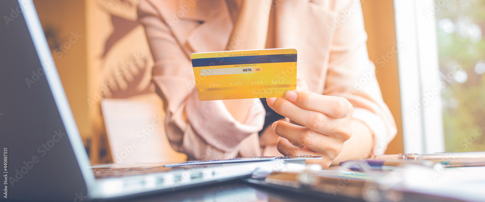 Women hold three credit cards to shop online with a laptop computer.