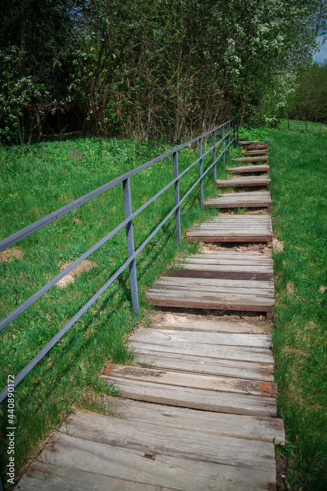 A wooden staircase with a metal railing leads up the slope of a grassy hill.