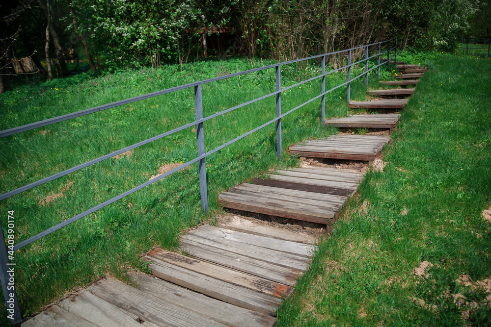 A wooden staircase with a metal railing leads up the slope of a grassy hill.