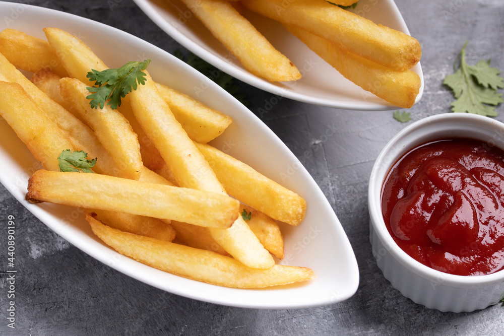 French fries with ketchup in white ceramic cup on gray background French fries with ketchup in white ceramic cup on gray background