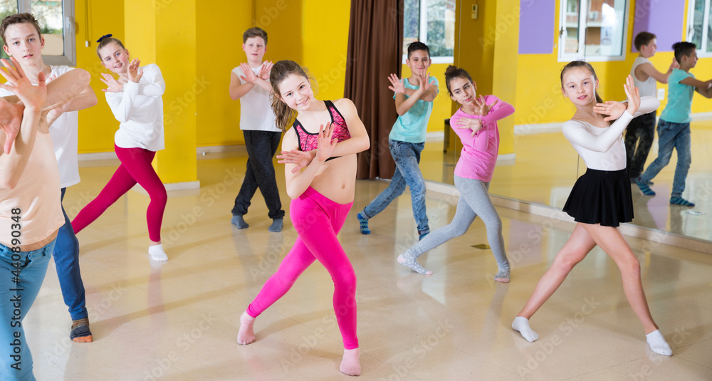 Teenage boys and girls practicing dance, stretching with female trainer in dance hall