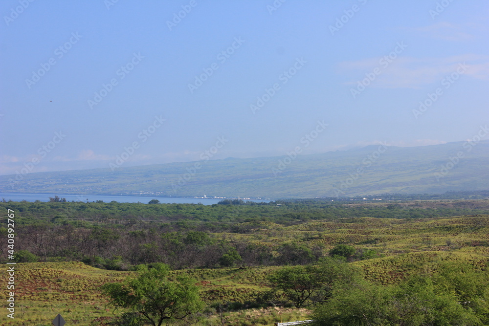 Fototapeta premium ハワイ島(ビッグアイランド)。緑の草に覆われた溶岩の大地と海に太陽の光が降り注ぐ。