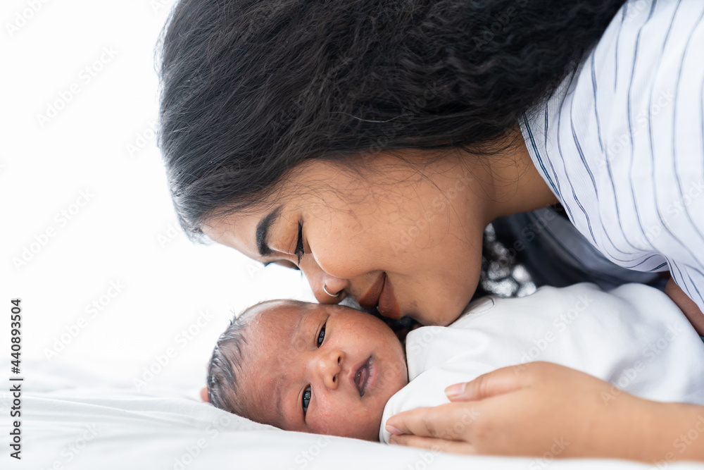 Mother kissing her newborn baby on the bed. Closeup of mom and infant baby Mother kissing her newborn baby on the bed. Closeup of mom and infant baby