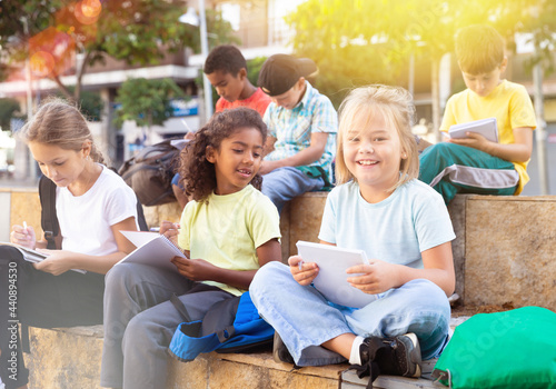 Smiling kids sitting on bench and writing in notepads, studying outdoors