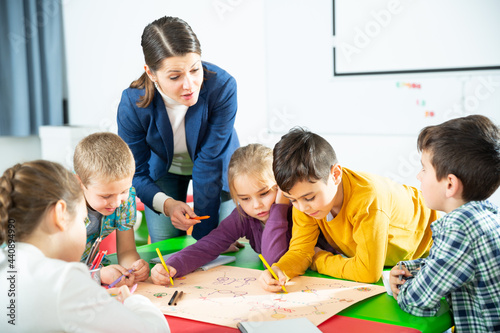 Pretty boys and girls with teacher draw a table game in classroom