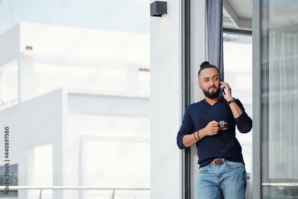 Pensive handsome bearded man drinking tea and talking on phone with friend or colleague Pensive handsome bearded man drinking tea and talking on phone with friend or colleague