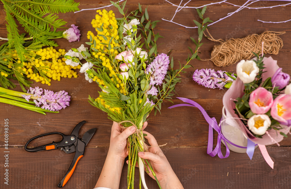 Florist at work: woman making fashion modern bouquet of different flowers on wooden background.