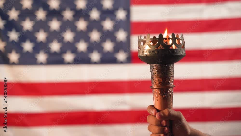 Close up of hands holding Olympic flame torch with US or American flag as background.