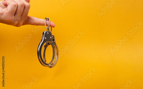 female hand holding handcuff with copy space on yellow background, illegal arrest