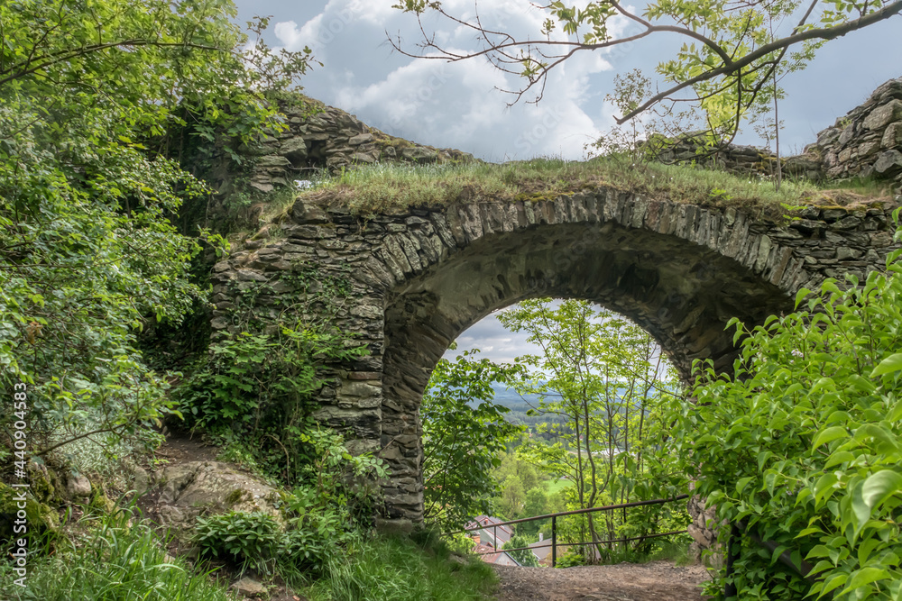 Old stone bridge in the mountains of the Czech Republic in the summer. Humpbacked bridge in greenery against the backdrop of a cloudy sky. Entrance to the dilapidated ancient castle on Mount Angela 