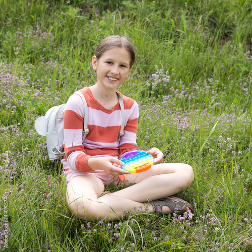 A little cute girl is sitting on the grass with a pop it - antistress toy. photo