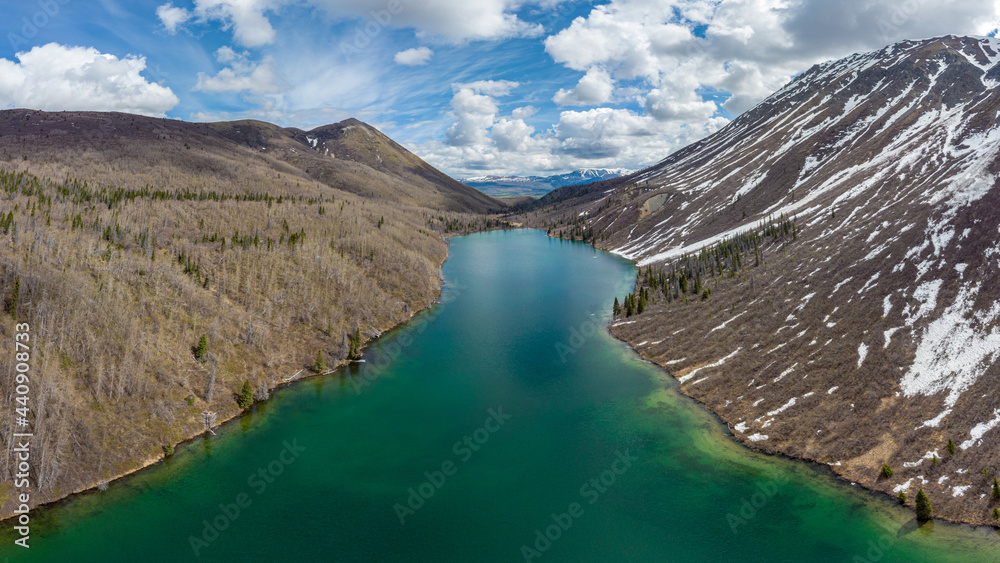 Stunning St Elias Lake in northern Canada during early summer time with emerald green lake below cascading mountain sides and blue sky with clouds. 