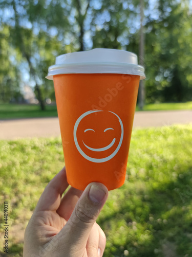 Disposable cup for coffee or tea in hand against the background of a summer landscape