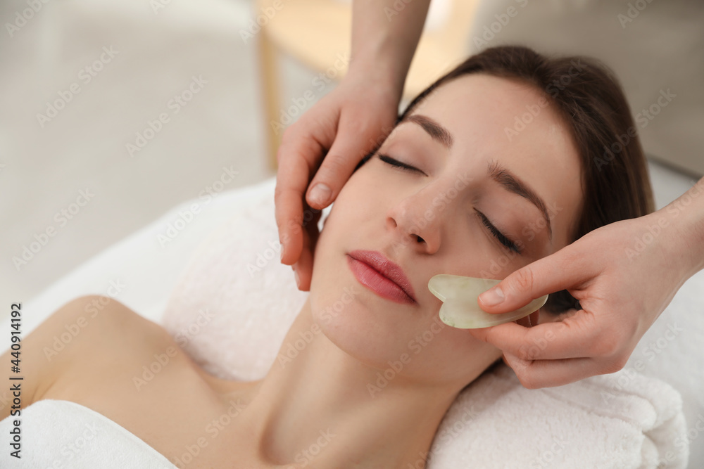 Young woman receiving facial massage with gua sha tool in beauty salon Young woman receiving facial massage with gua sha tool in beauty salon