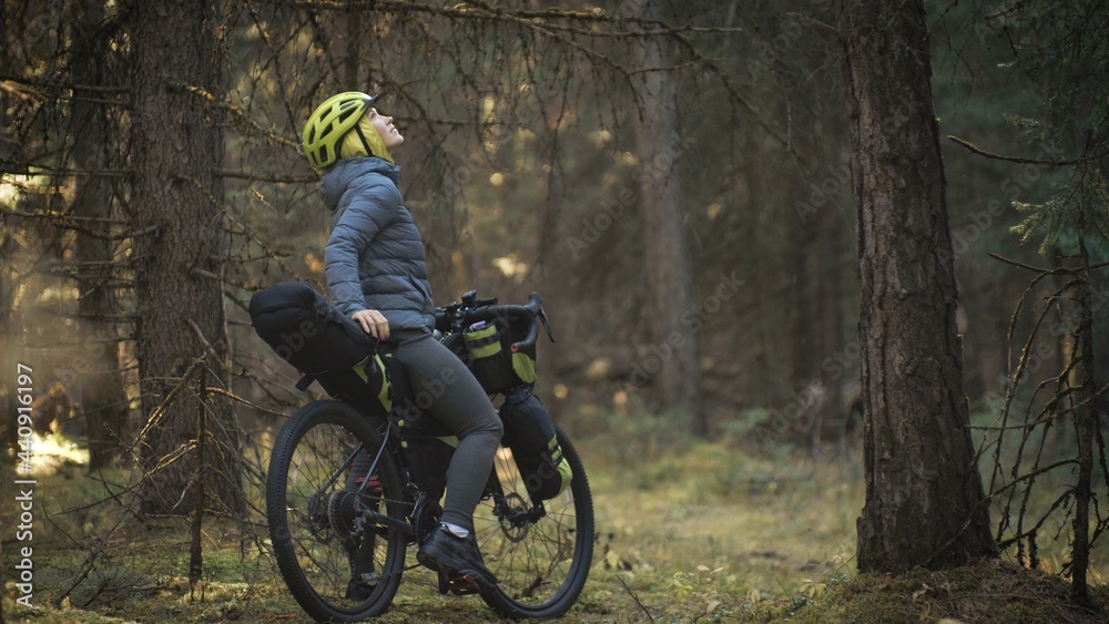Obraz premium The woman travel on mixed terrain cycle touring with bike bikepacking outdoor. The traveler journey with bicycle bags. Stylish bikepacking, bike, sportswear in green black colors. Magic forest park.