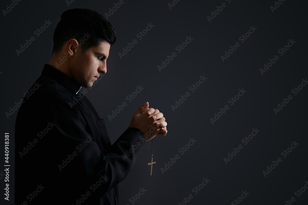Priest with cross praying on black background. Space for text Priest with cross praying on black background. Space for text