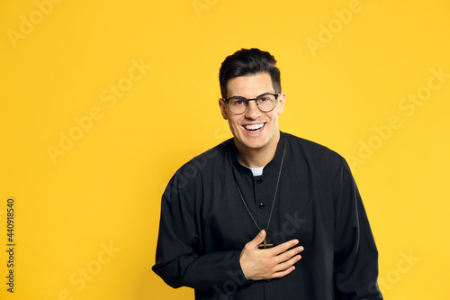 Φωτογραφία Priest in cassock with clerical collar laughing on yellow background